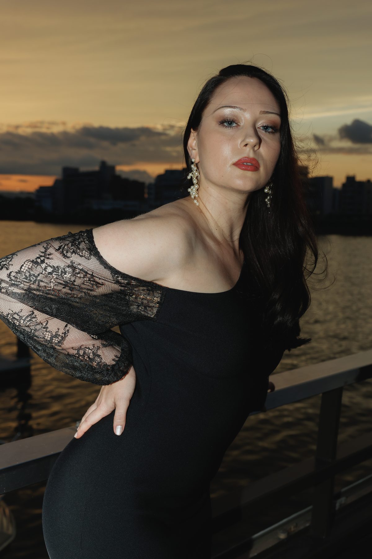 夕暮れの水辺で、レースの袖の黒いドレスを着た女性が振り返る