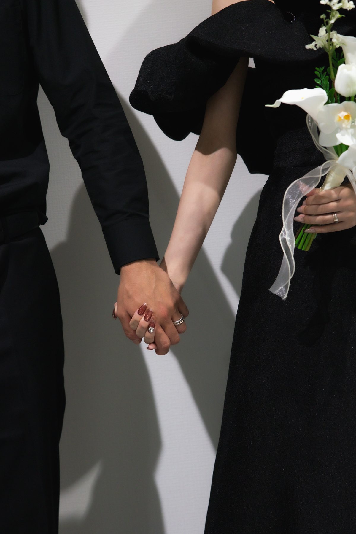 黒い服で手をつなぐカップル。花束と指輪